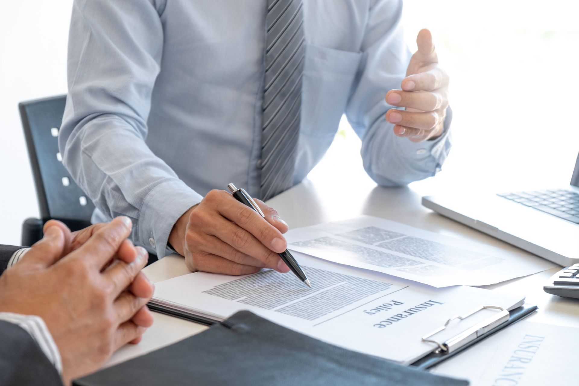 Two people in business attire reviewing documents at a desk; one points, one holds a pen.
