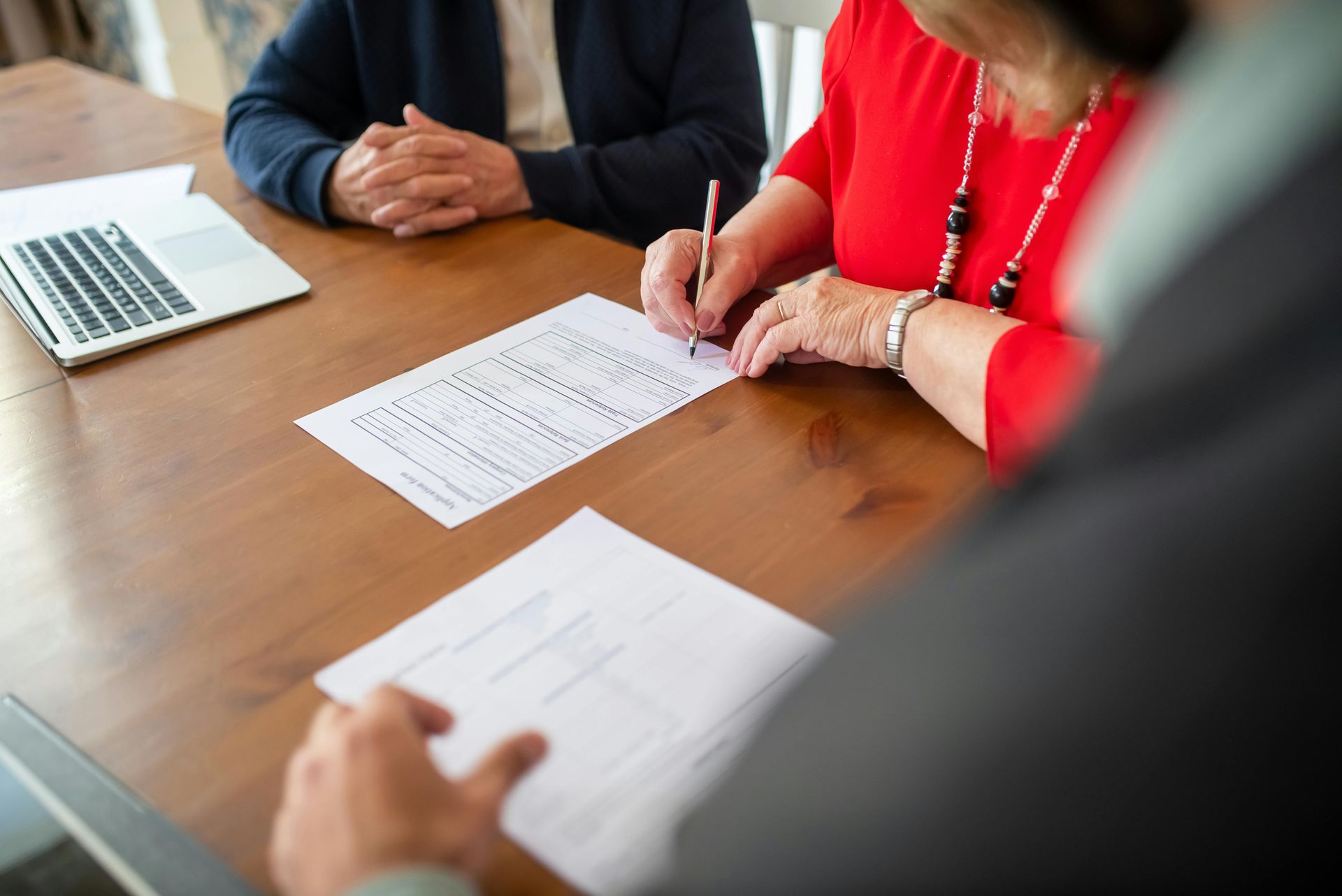Person signing a document at a table, with two other people present.