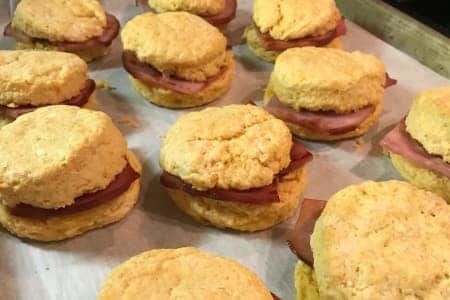 Biscuits with sliced ham on a baking sheet. Golden biscuits, ham visible between halves.