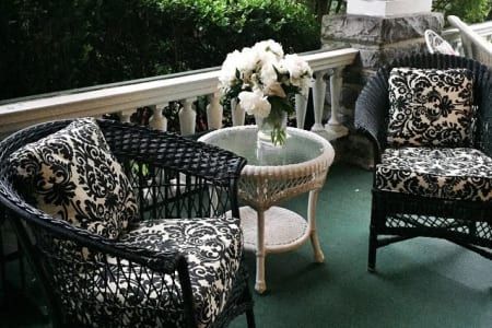 Wicker chairs with patterned cushions, small table with flowers, on a porch with white railing.