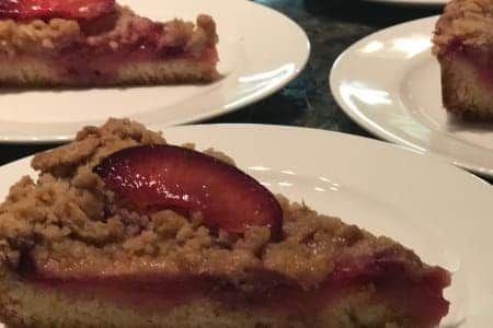 Slices of plum crumble cake on white plates.