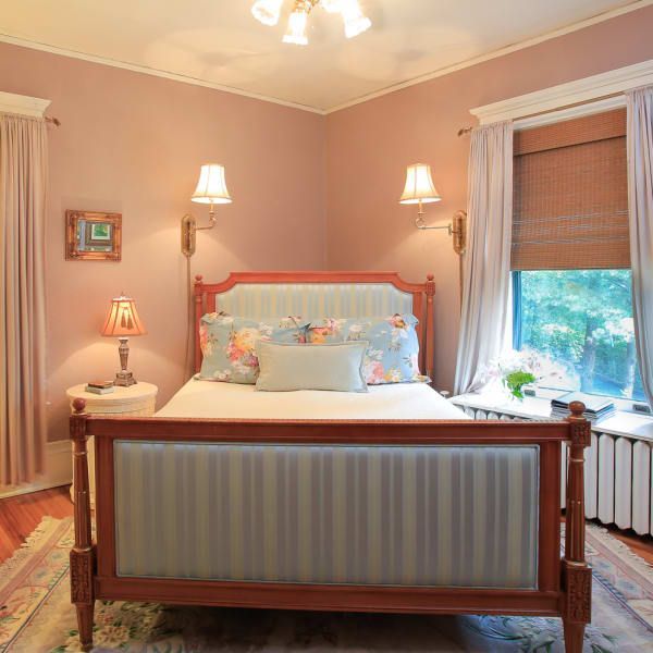 Bedroom with pink walls, wood bed, floral bedding, window with blinds, and side lamps.