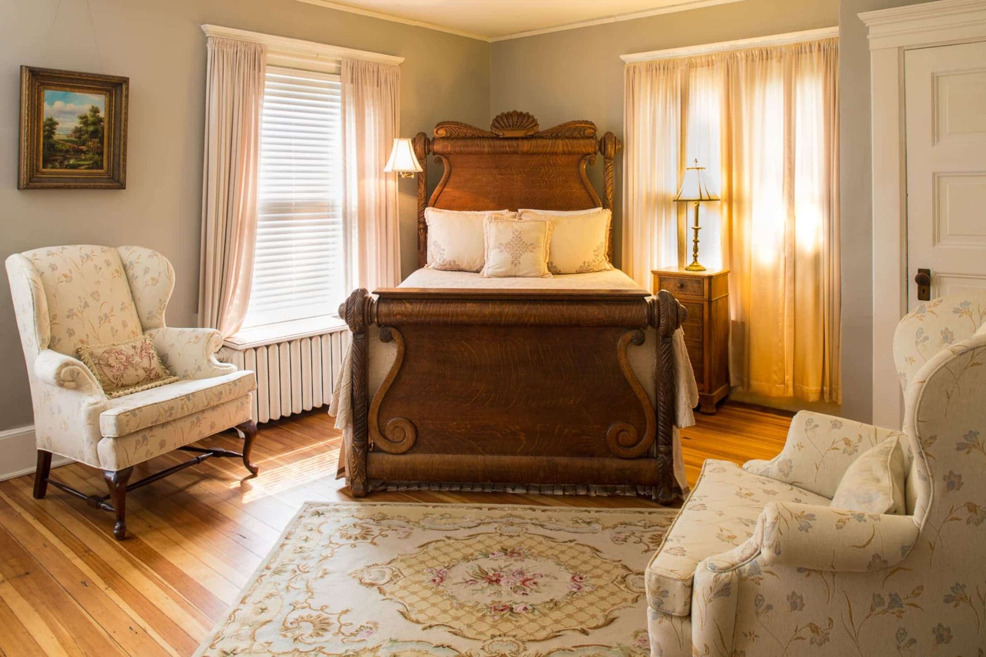 Bedroom with ornate wooden bed, floral chairs, window with curtains, and rug.
