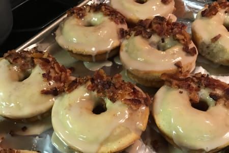 Glazed donuts with bacon pieces on a metal tray.