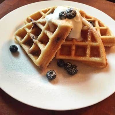Waffles with blueberries and whipped cream on a white plate.