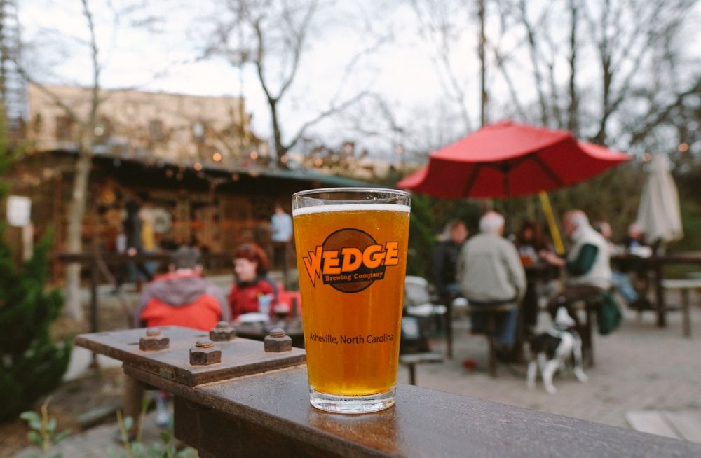 Beer glass at Wedge Brewery outdoor patio with people and red umbrella.