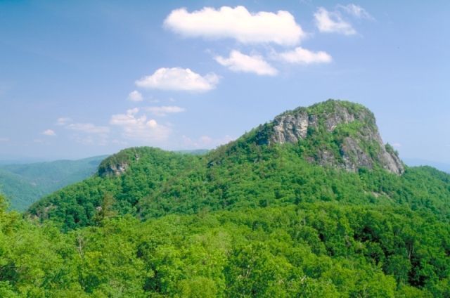 Green, forested mountain under a blue sky with puffy white clouds.
