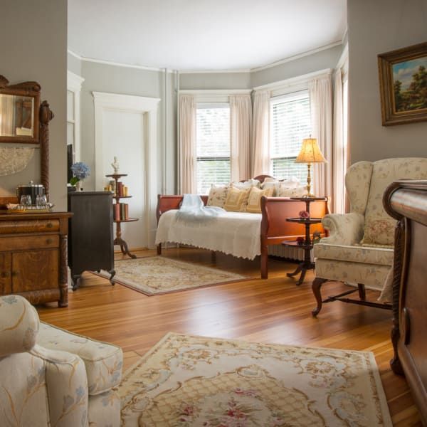 Elegant bedroom with hardwood floors, bay window, antique furniture, and rugs.