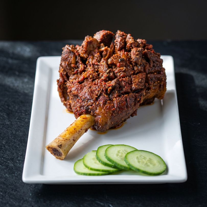 Braised meat shank on a white plate with cucumber slices on a dark background