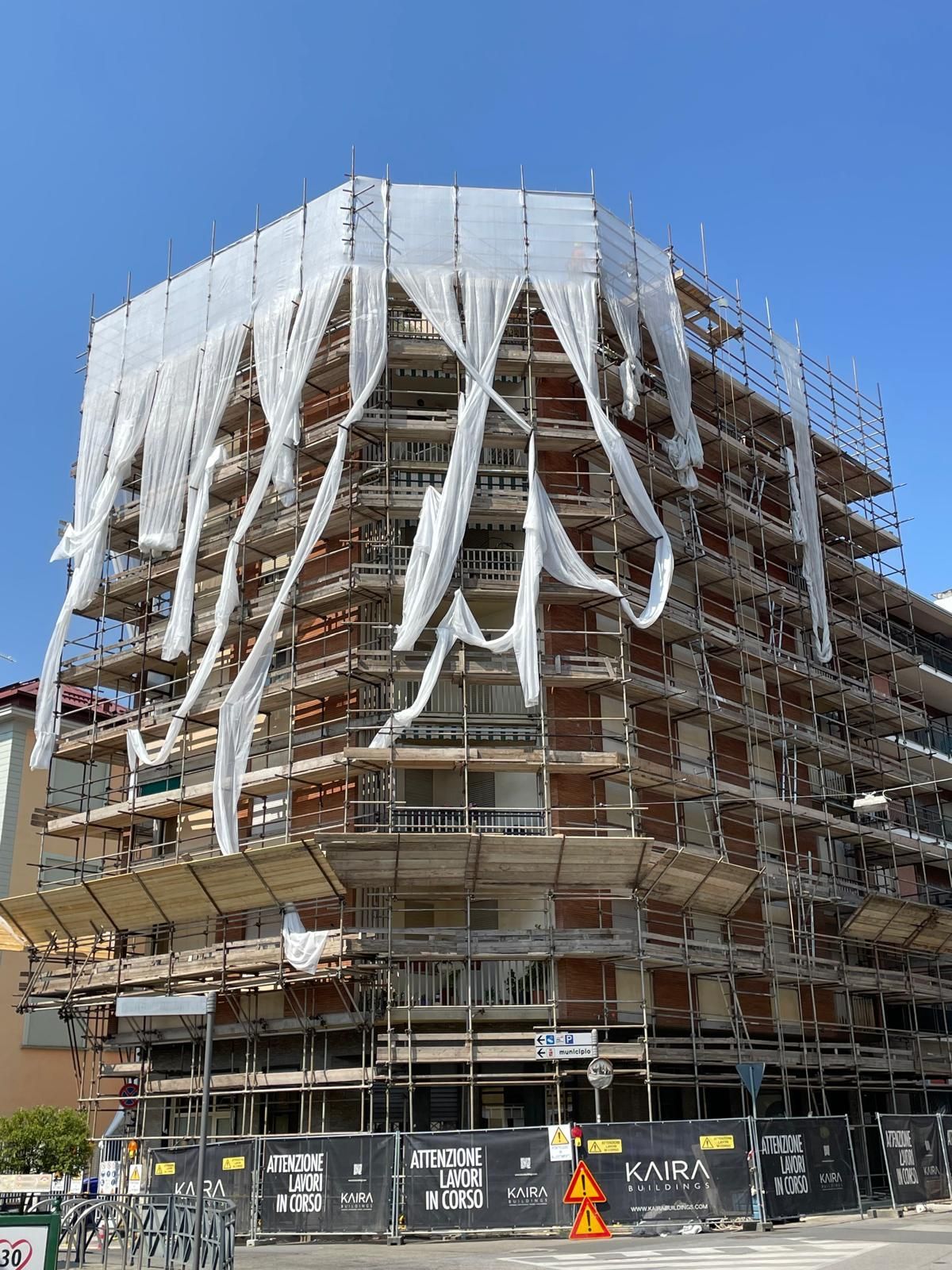 Edificio multipiano in costruzione, parzialmente avvolto da teli protettivi bianchi e impalcature.