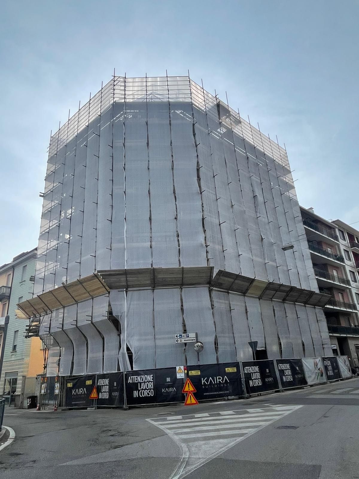 Edificio a più piani in costruzione, avvolto da una rete di impalcature bianca, all'angolo di una strada.
