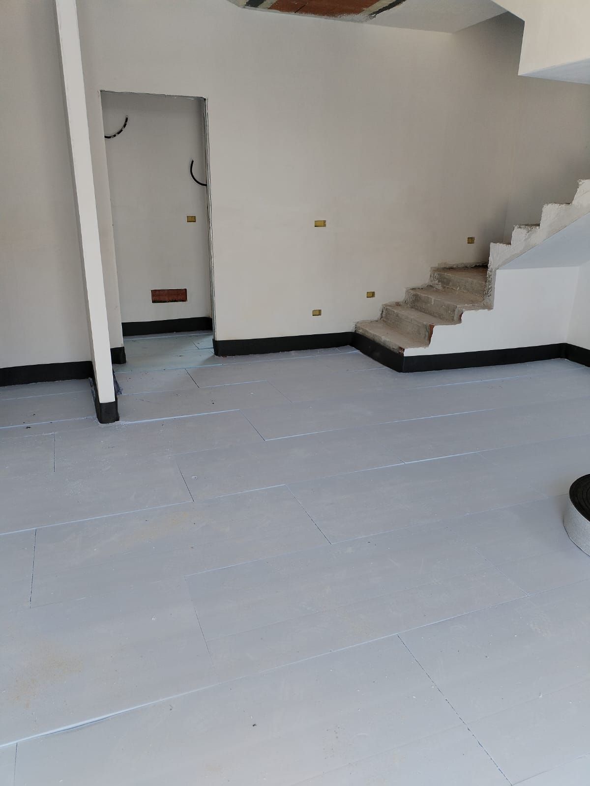 Stanza vuota con pareti bianche, pavimento grigio, porta aperta e scale sulla destra.