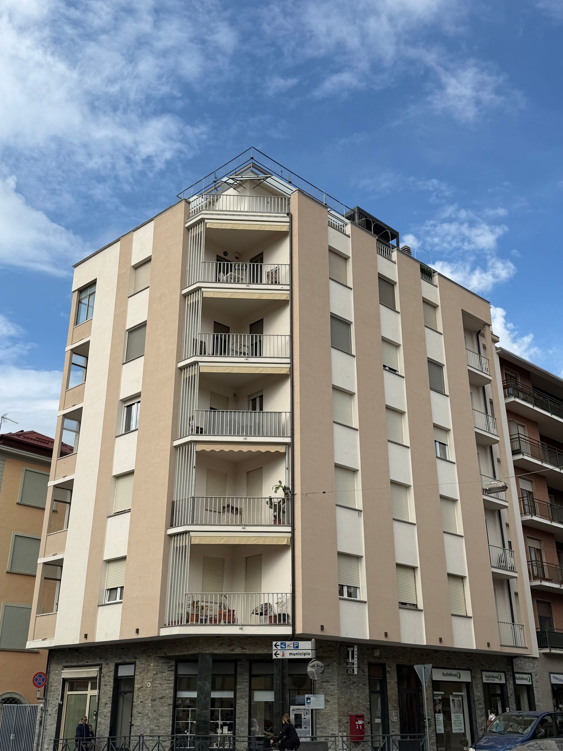 Alto palazzo beige con balconi, situato all'angolo di una strada sotto un cielo azzurro.