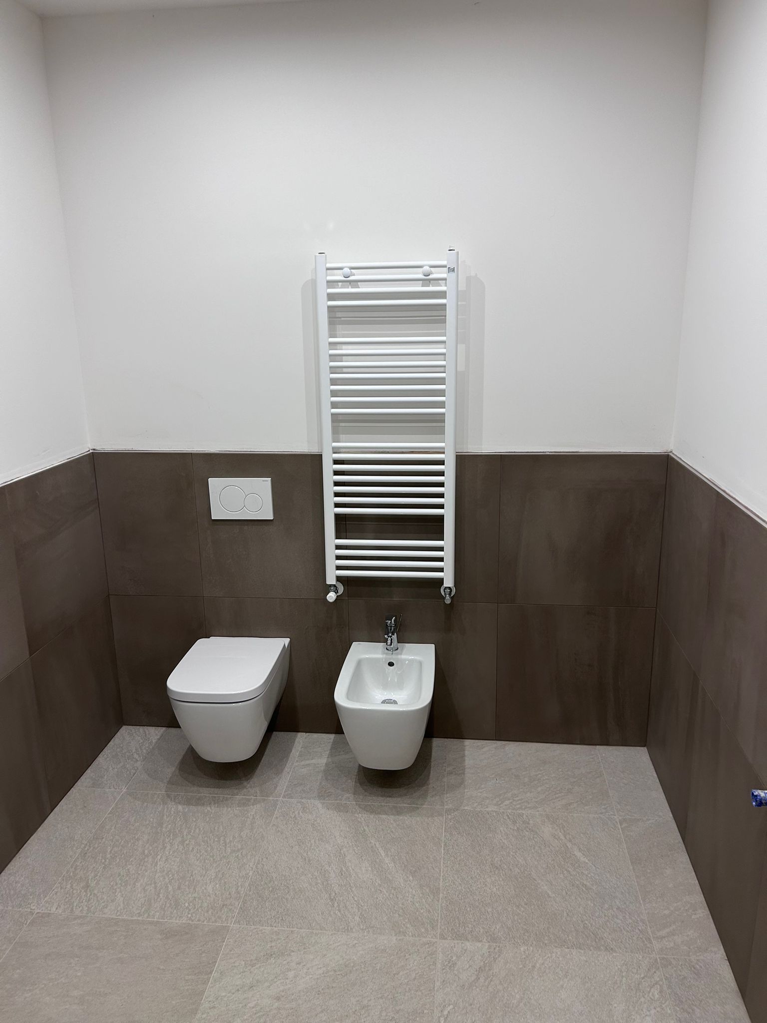 Bagno accessibile con WC, bidet, termosifone a parete e pareti rivestite con piastrelle marroni.