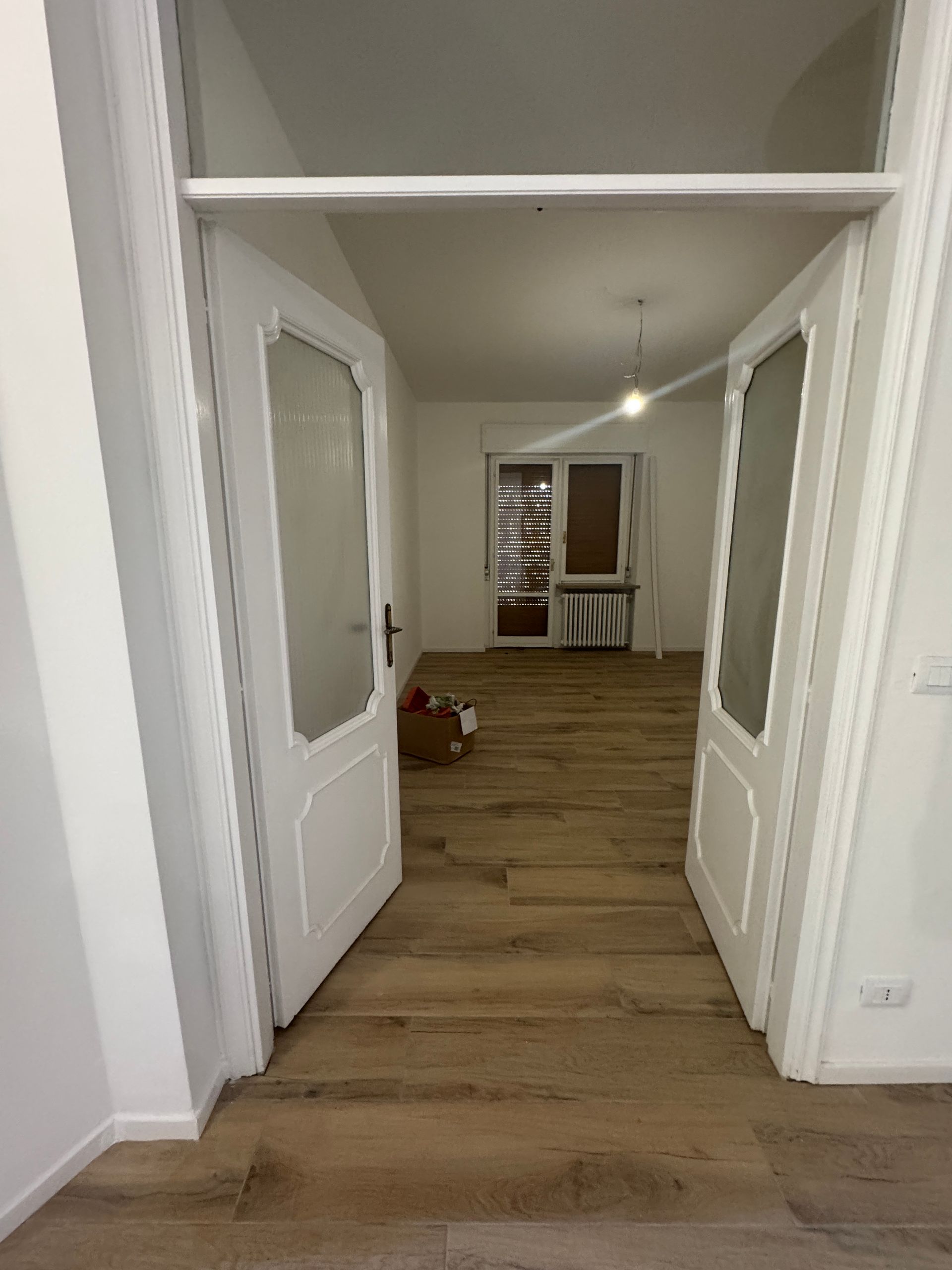 Apri le doppie porte bianche che conducono a una stanza con pavimento in legno e una sedia in fondo.