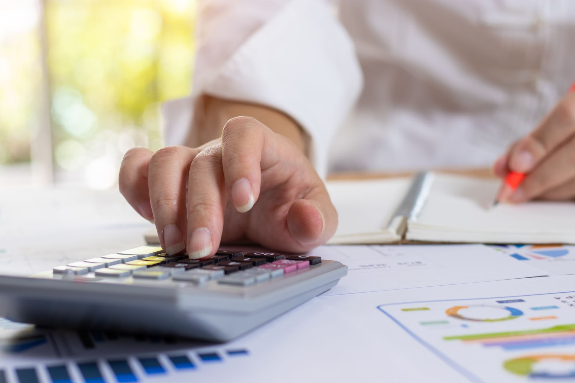 A person is using a calculator and writing in a notebook.
