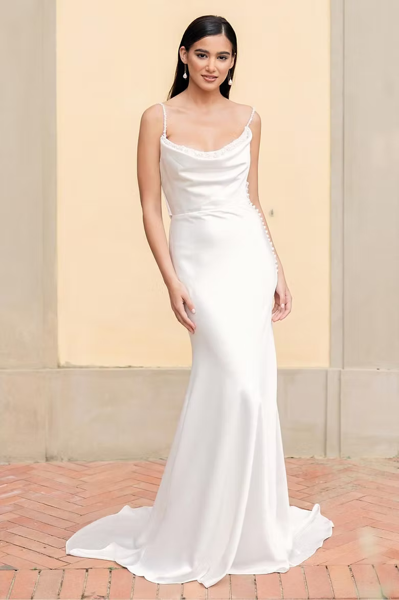 Woman in a white satin wedding dress with a cowl neck, standing outdoors.