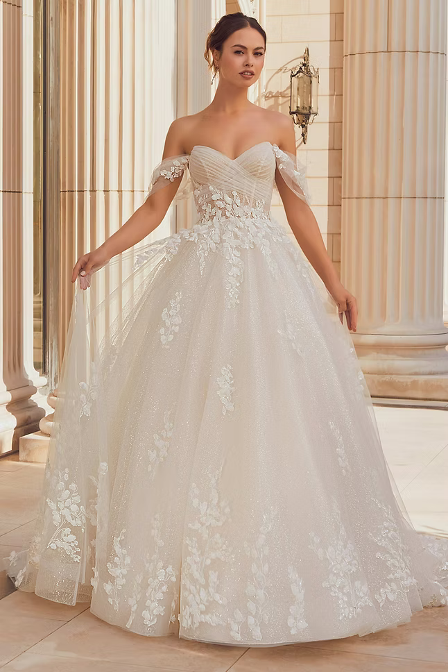 Woman in a white off-the-shoulder wedding dress, standing near columns.