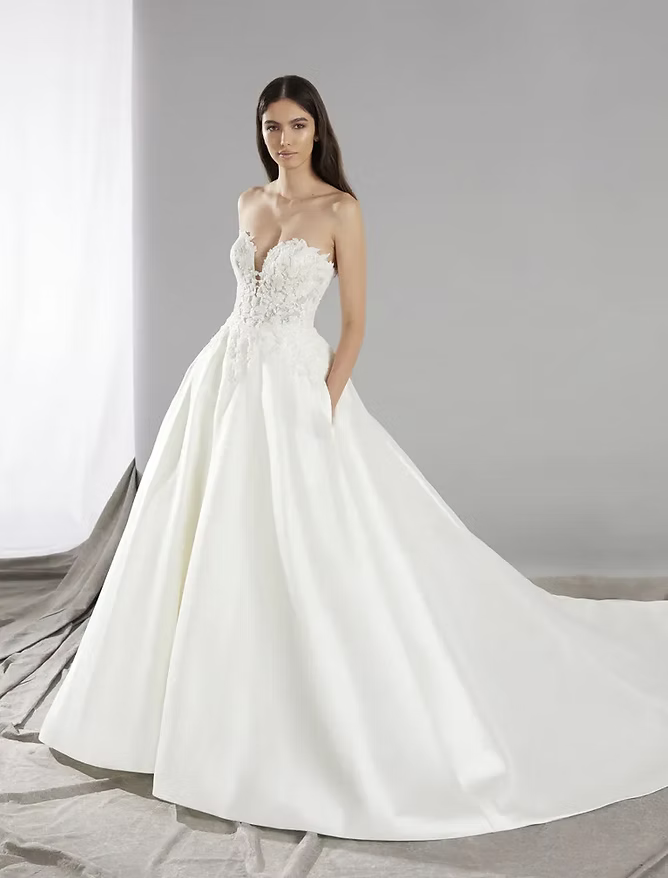 Woman in a strapless white ball gown with pockets, train, and detailed bodice.