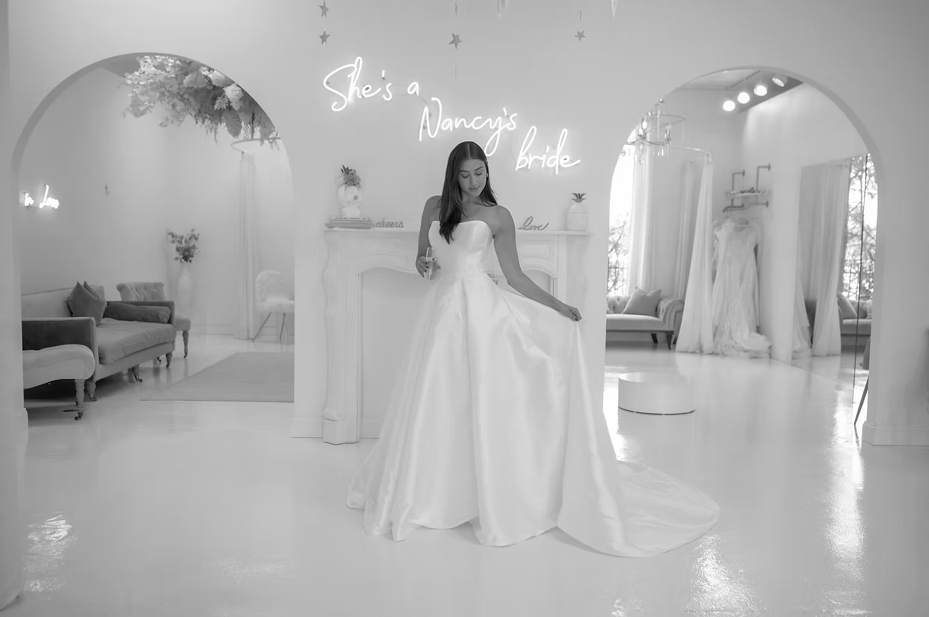 Woman in wedding dress poses in a bridal shop with a neon sign that says