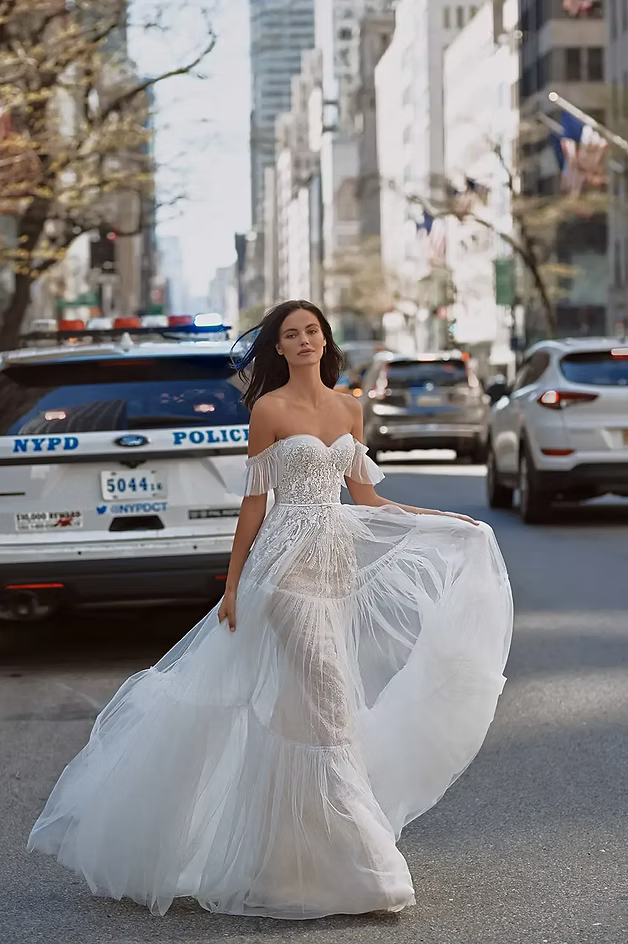 Woman in wedding dress poses in a city street with a police car in the background.