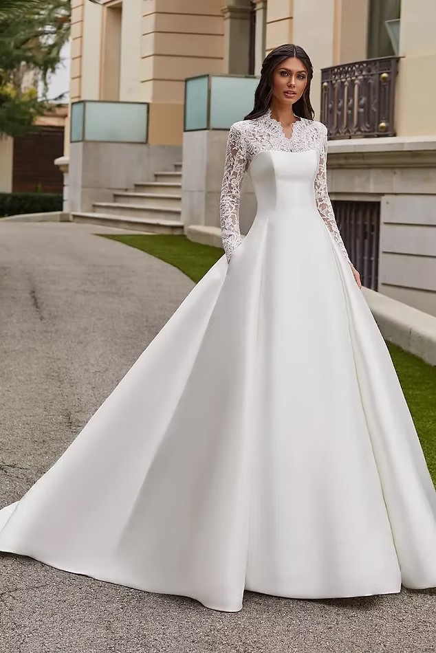 Woman in white wedding dress with long train, lace sleeves, outdoors.
