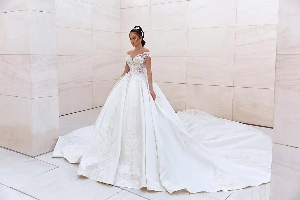 Bride in a white ballgown with long train, posing in a white-walled room.