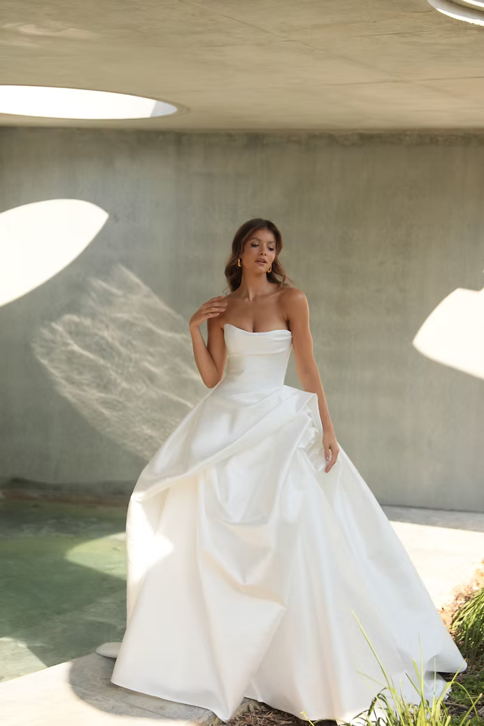 Woman in strapless white wedding dress, standing outdoors.