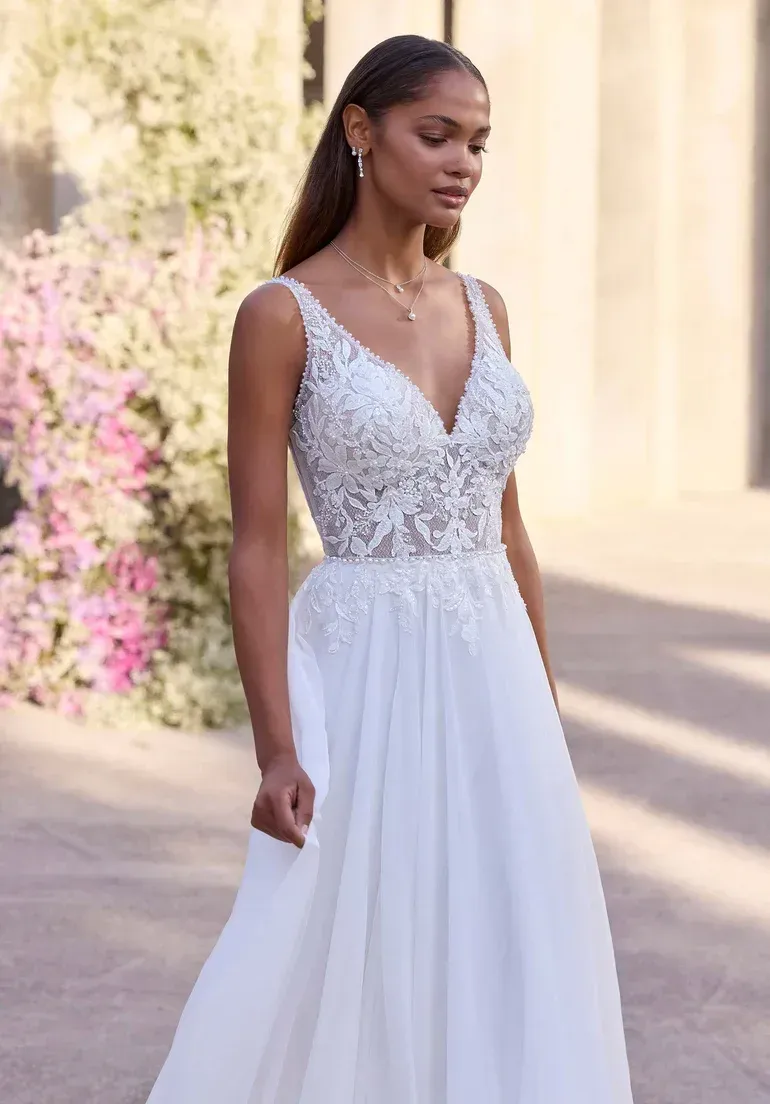 Woman in white wedding dress, floral bodice, flowing skirt, outdoor setting.