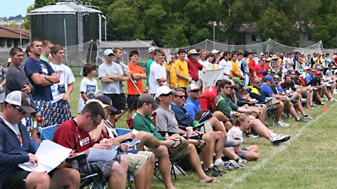 A large group of people are sitting on a field watching a game.