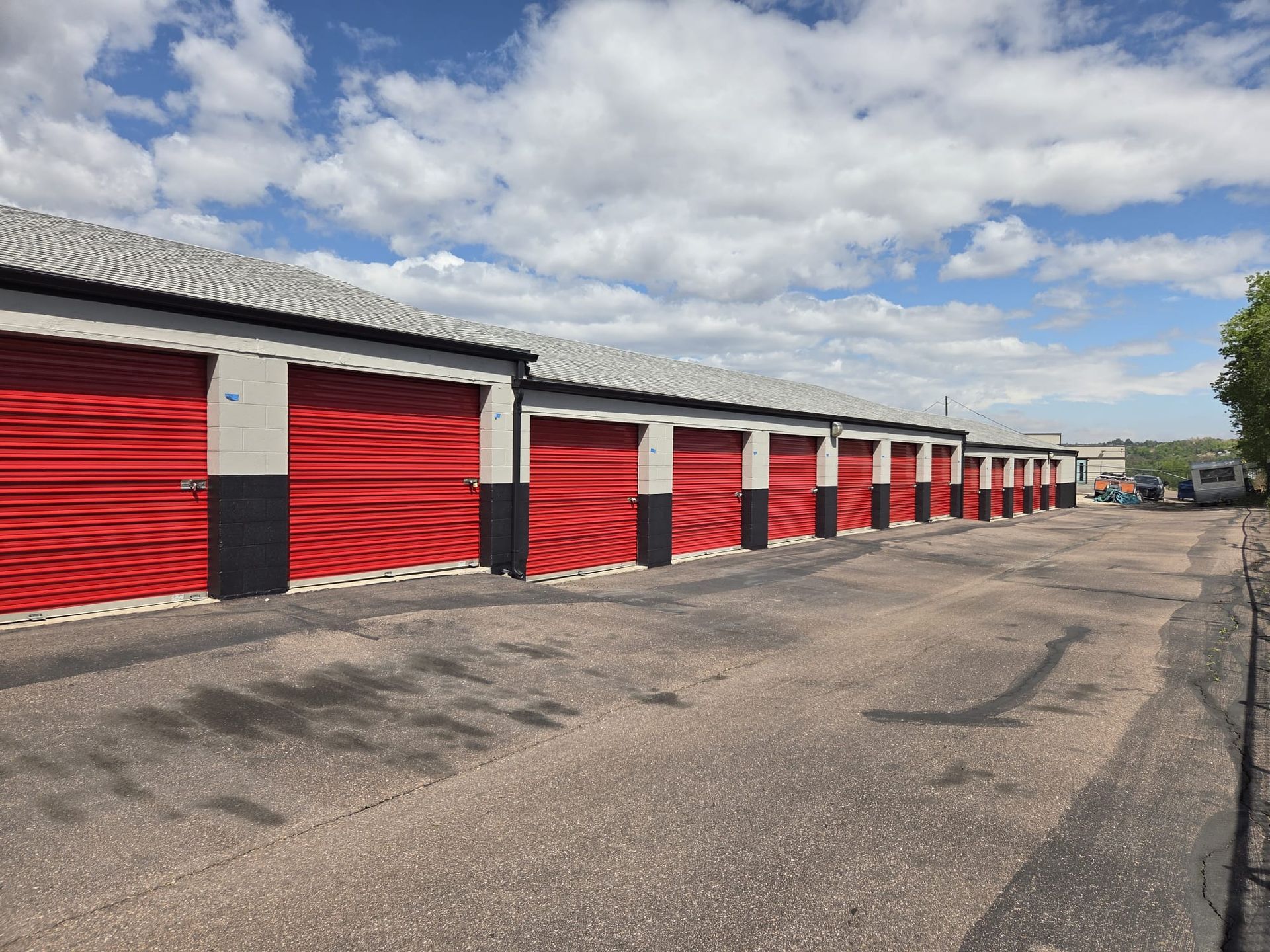Row of red storage unit doors along a paved lot under a cloudy sky