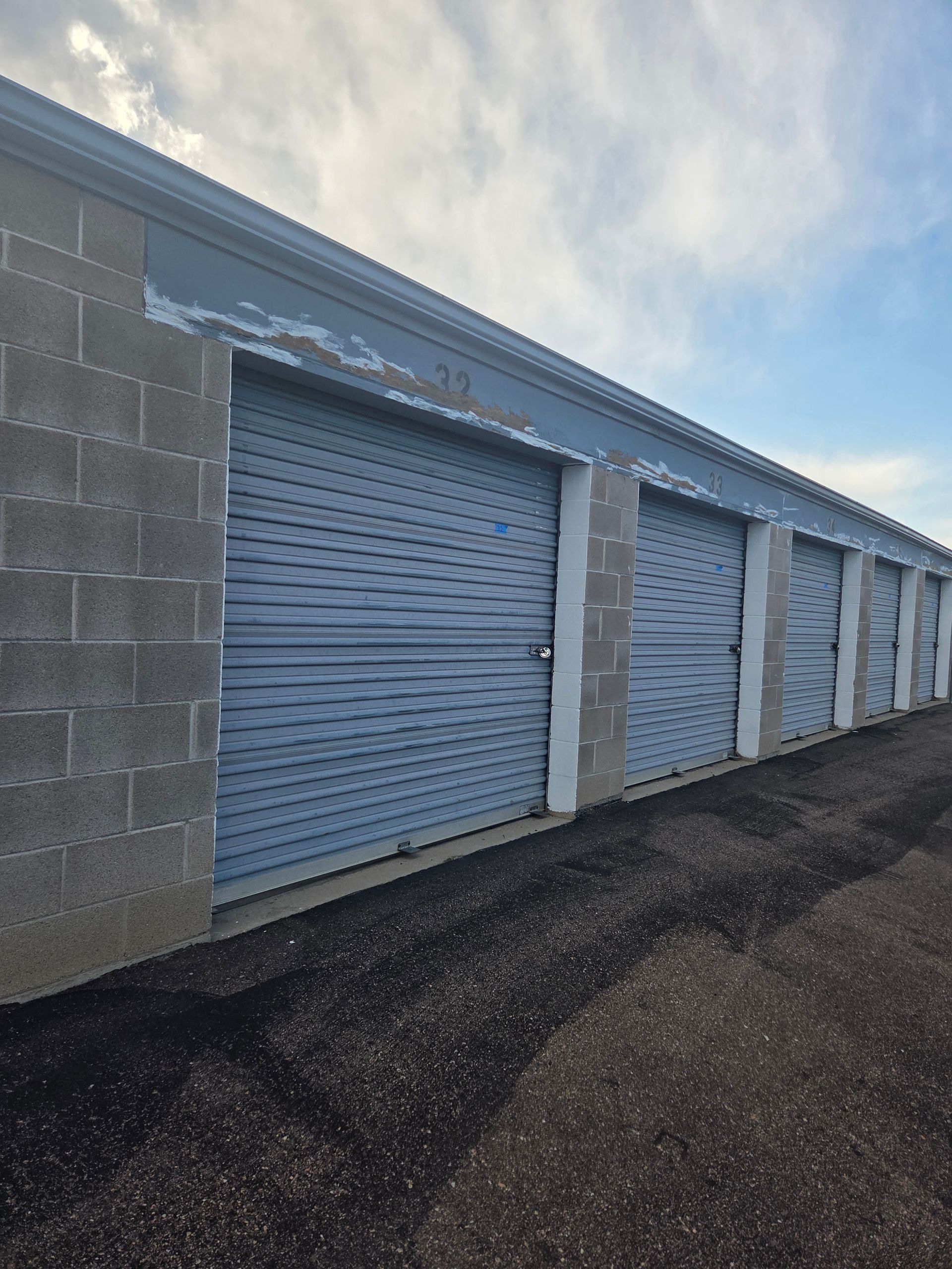 Row of blue storage unit doors beside a cinder block wall on a paved lot.
