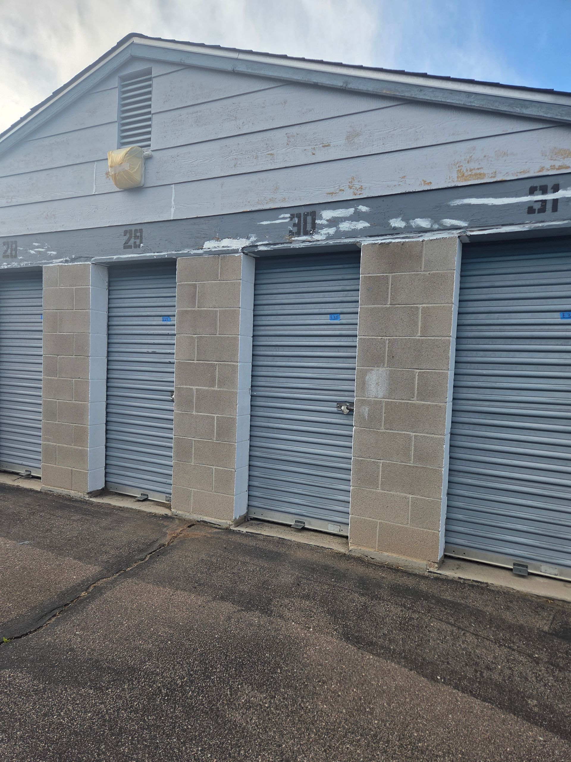 Row of blue-gray storage unit doors with concrete pillars and a sloped roof exterior