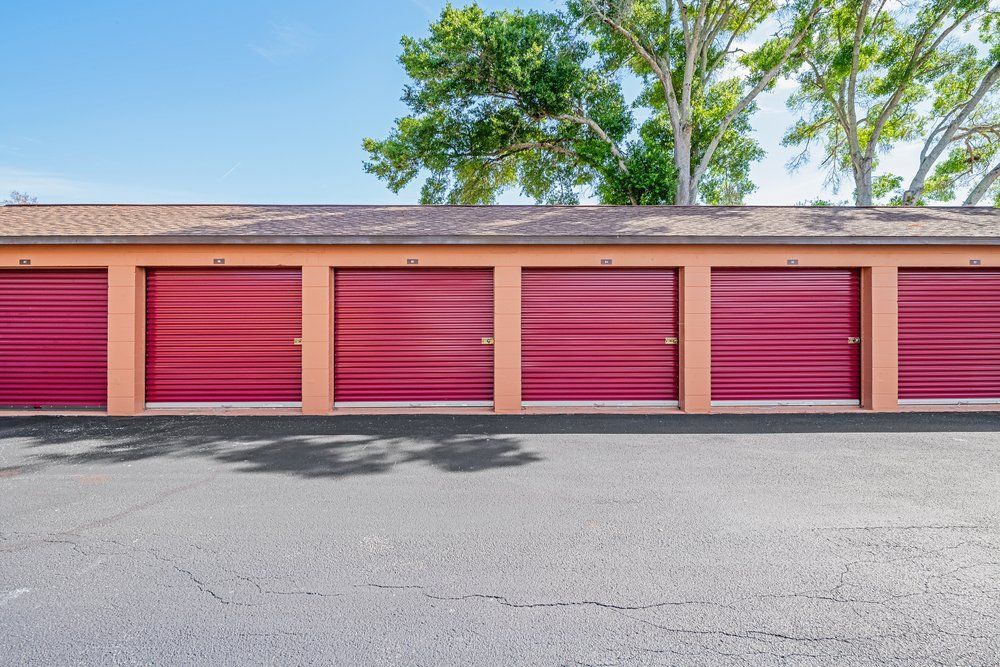 Row of pink storage unit doors on a beige building with trees above and asphalt foreground
