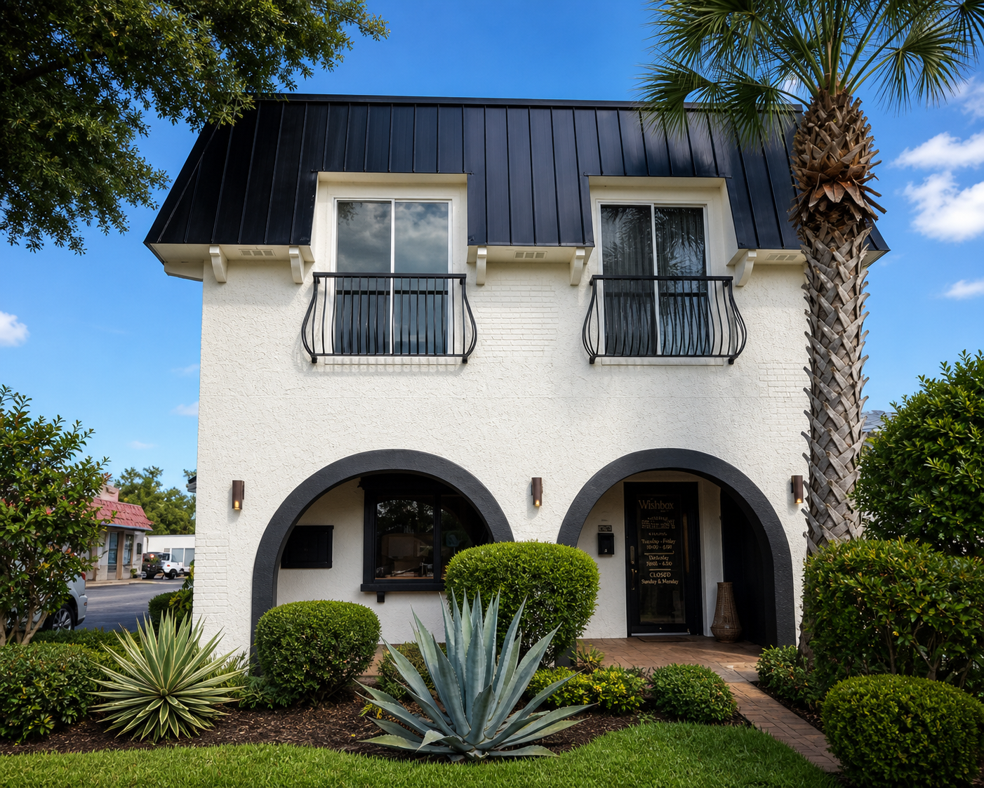 White two-story house with black roof, arched entry, and landscaped front yard with palm trees.