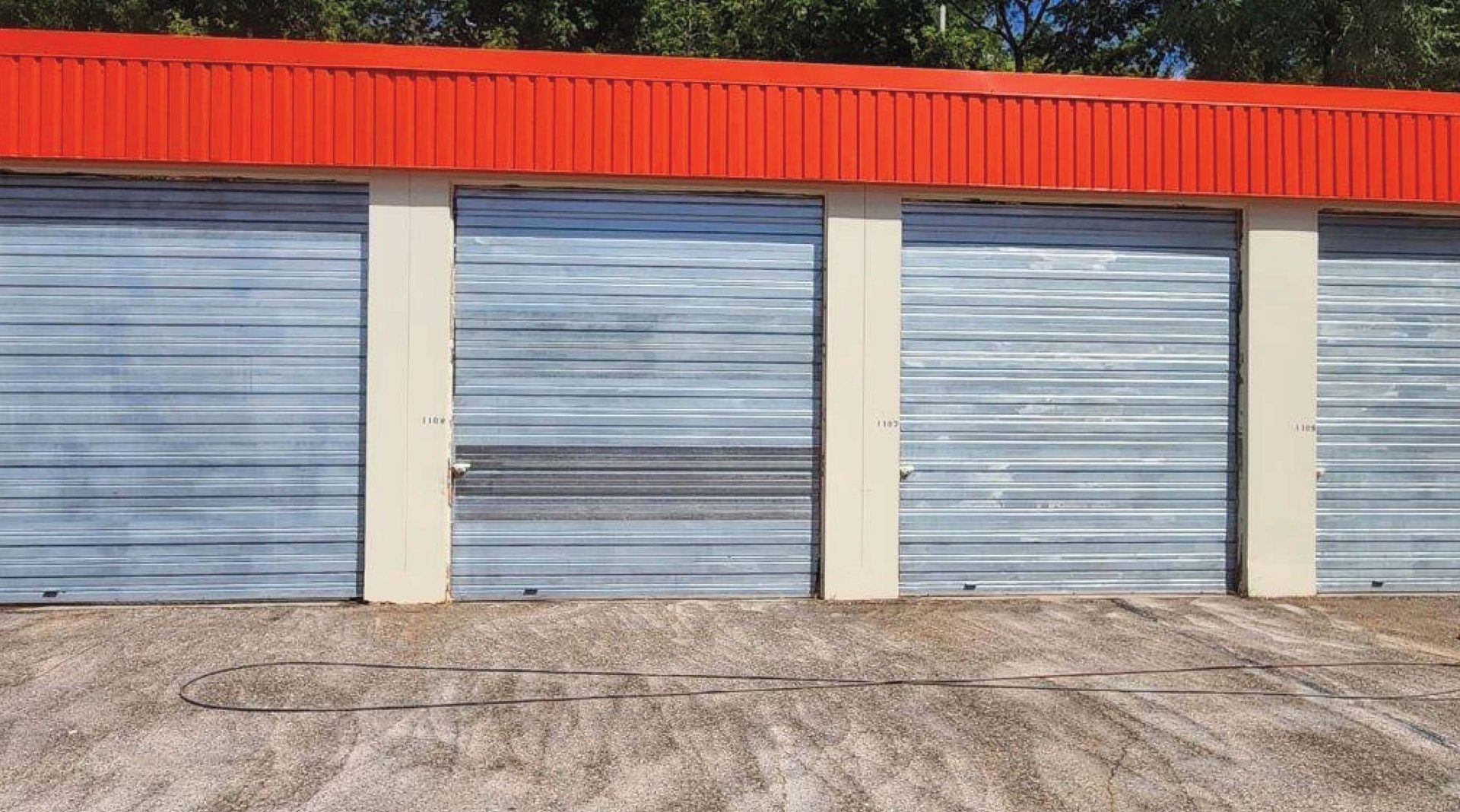 Row of blue metal garage doors with beige pillars and a red corrugated roof