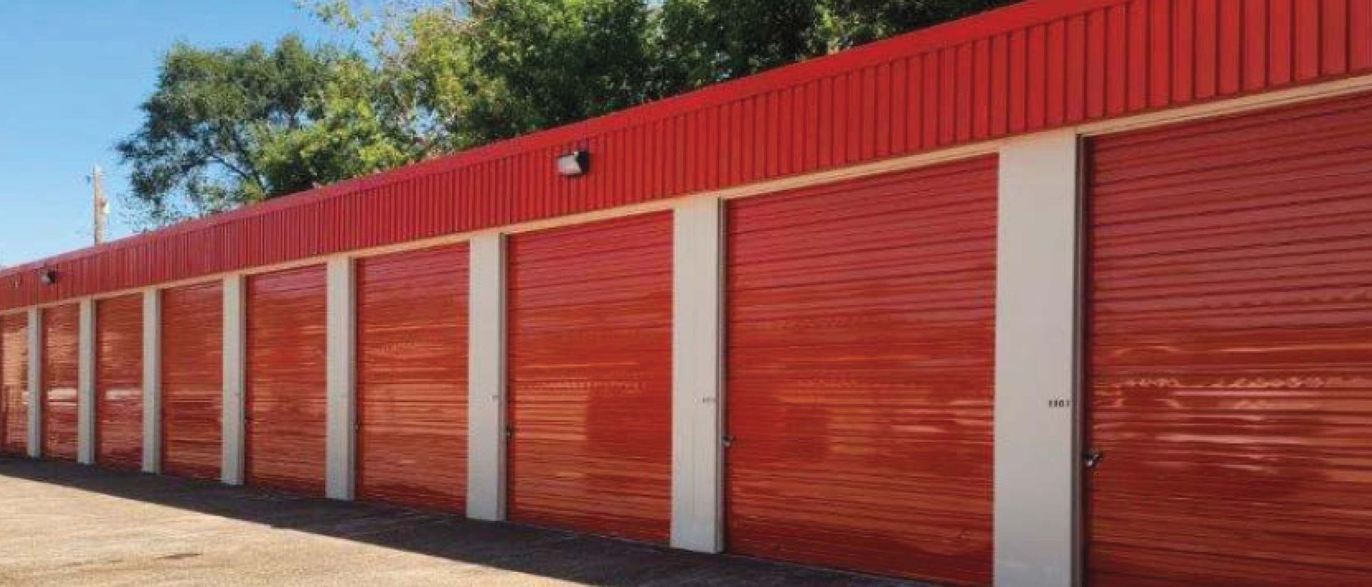Row of blue metal garage doors with beige pillars and a red corrugated roof