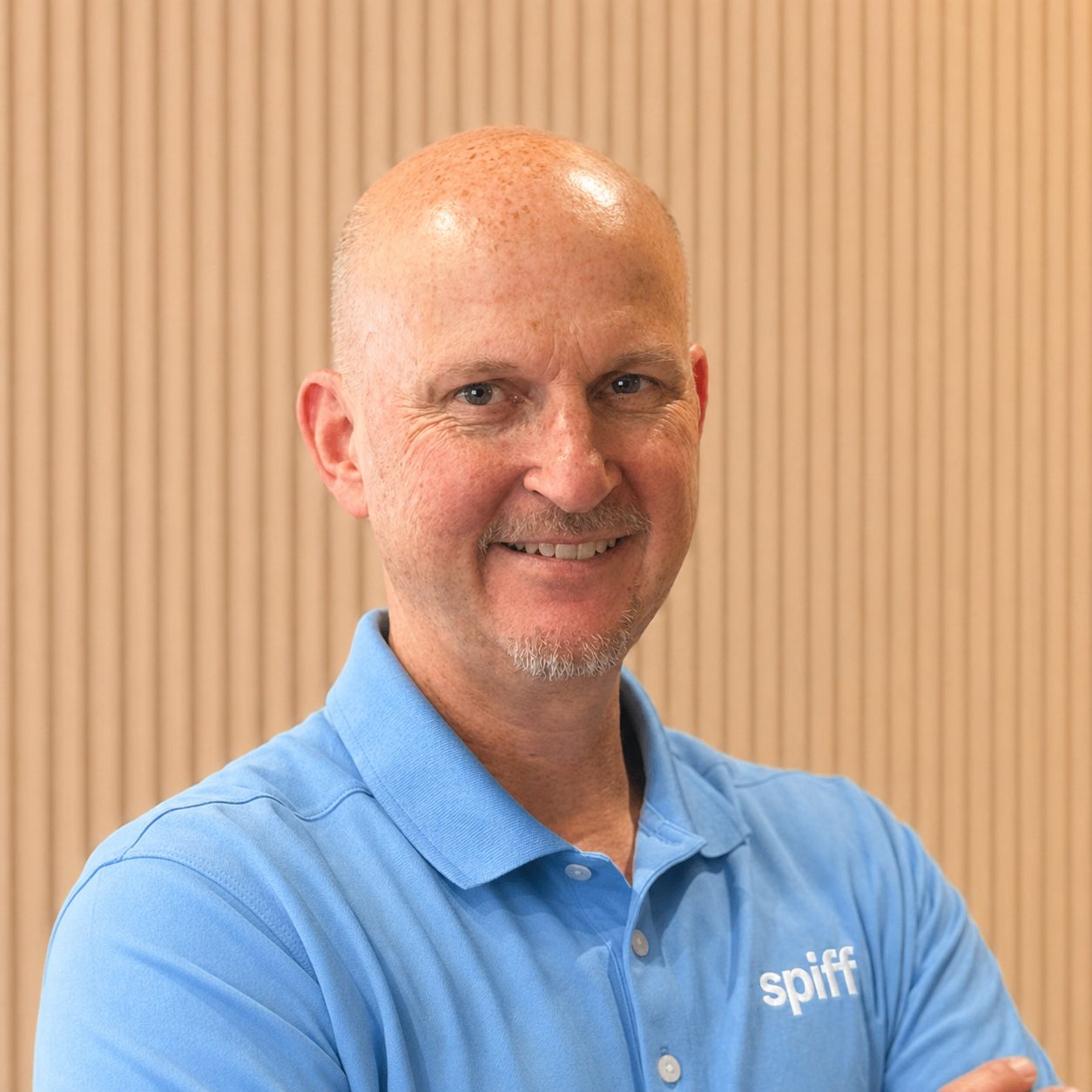 Smiling bald man in a blue polo shirt against a beige striped background