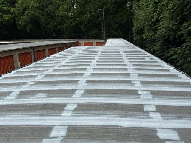 White corrugated roof with painted seams stretching toward red garages and trees