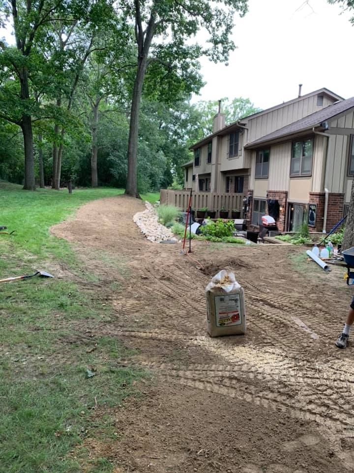 Backyard landscape project with dirt, trees, and a house. A bag of material sits in the dirt.