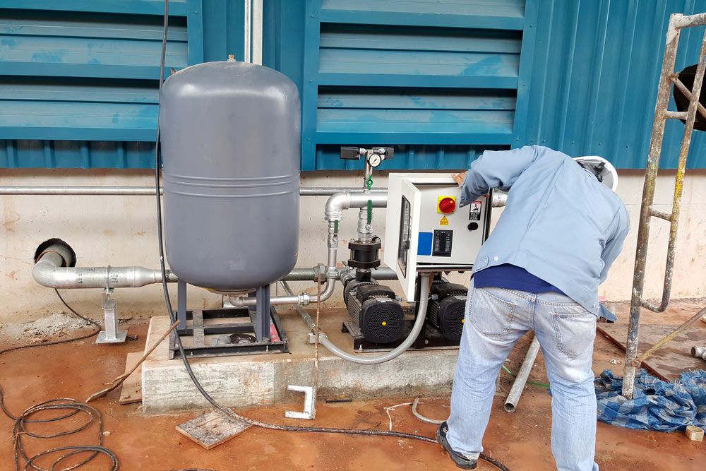 A Man is Working on a Water Pump Outside of a Building — Himec Electrical In Gatton, QLD