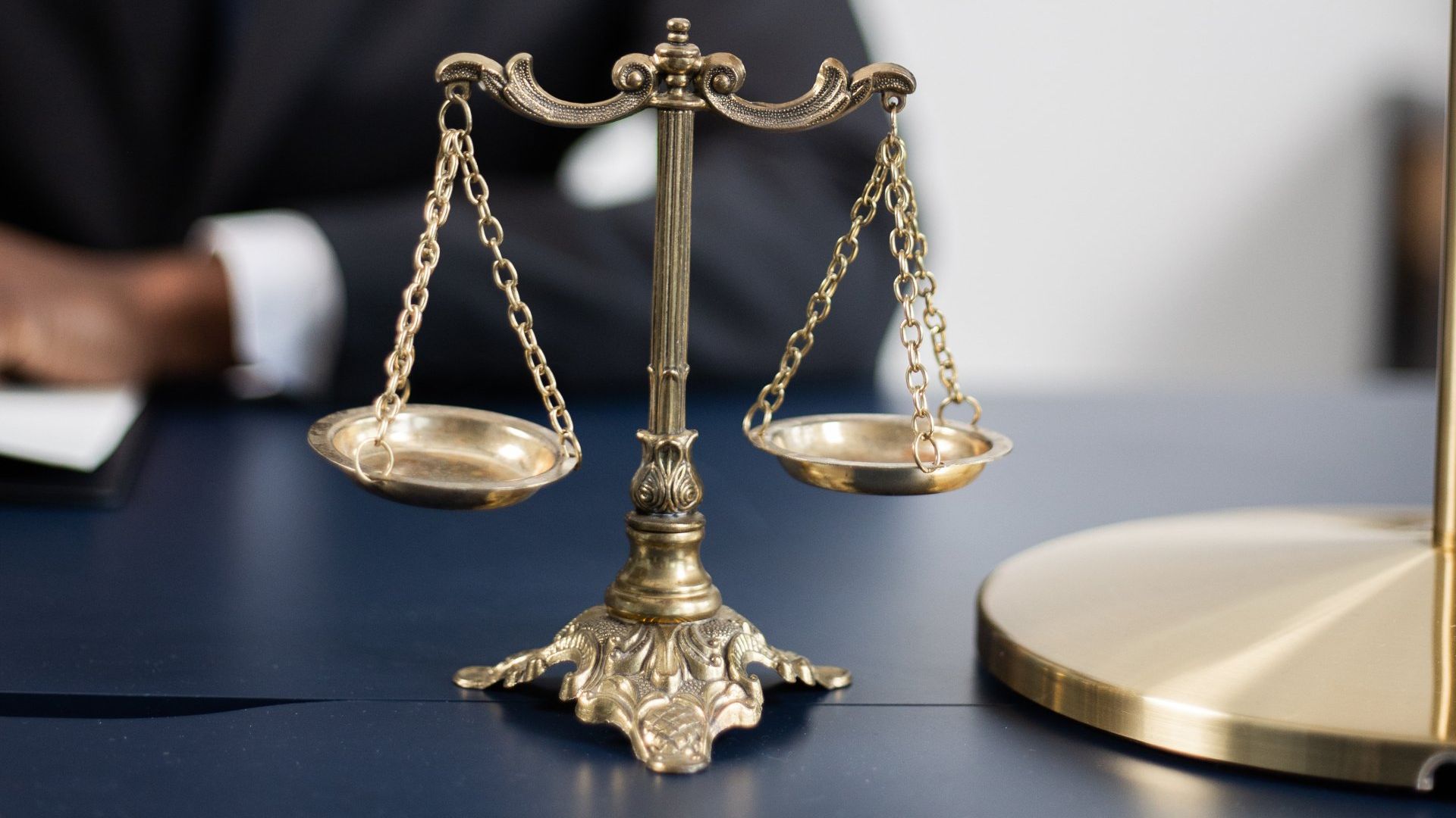 A scale of justice is on a table with a man in the background.