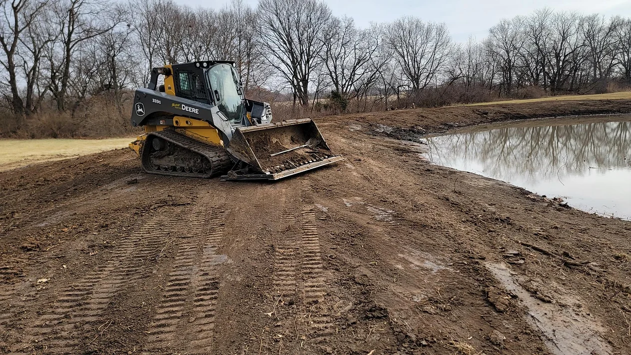 a bulldozer is driving through a muddy field next to a body of water .