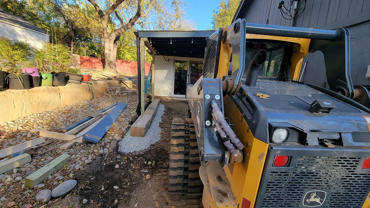 A yellow and black bulldozer is parked on a dirt road next to a house under construction.