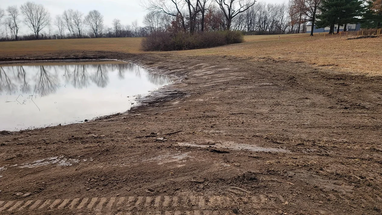 a muddy field with a pond in the middle of it .