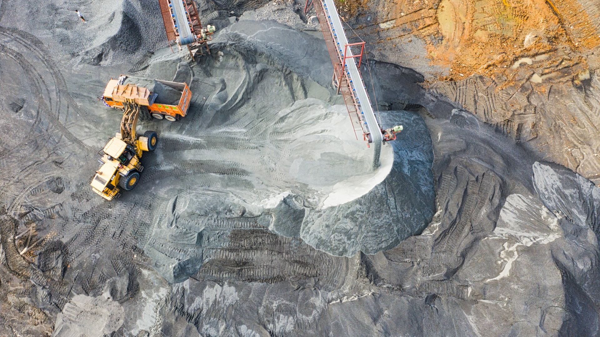An aerial view of a quarry with a bulldozer and a conveyor belt.