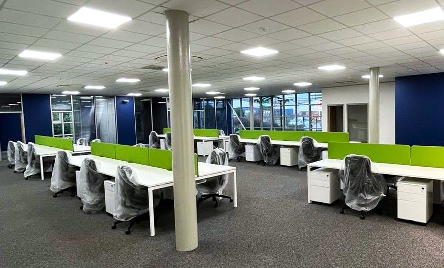 Empty office with rows of white desks, green dividers, gray chairs, and gray carpet.