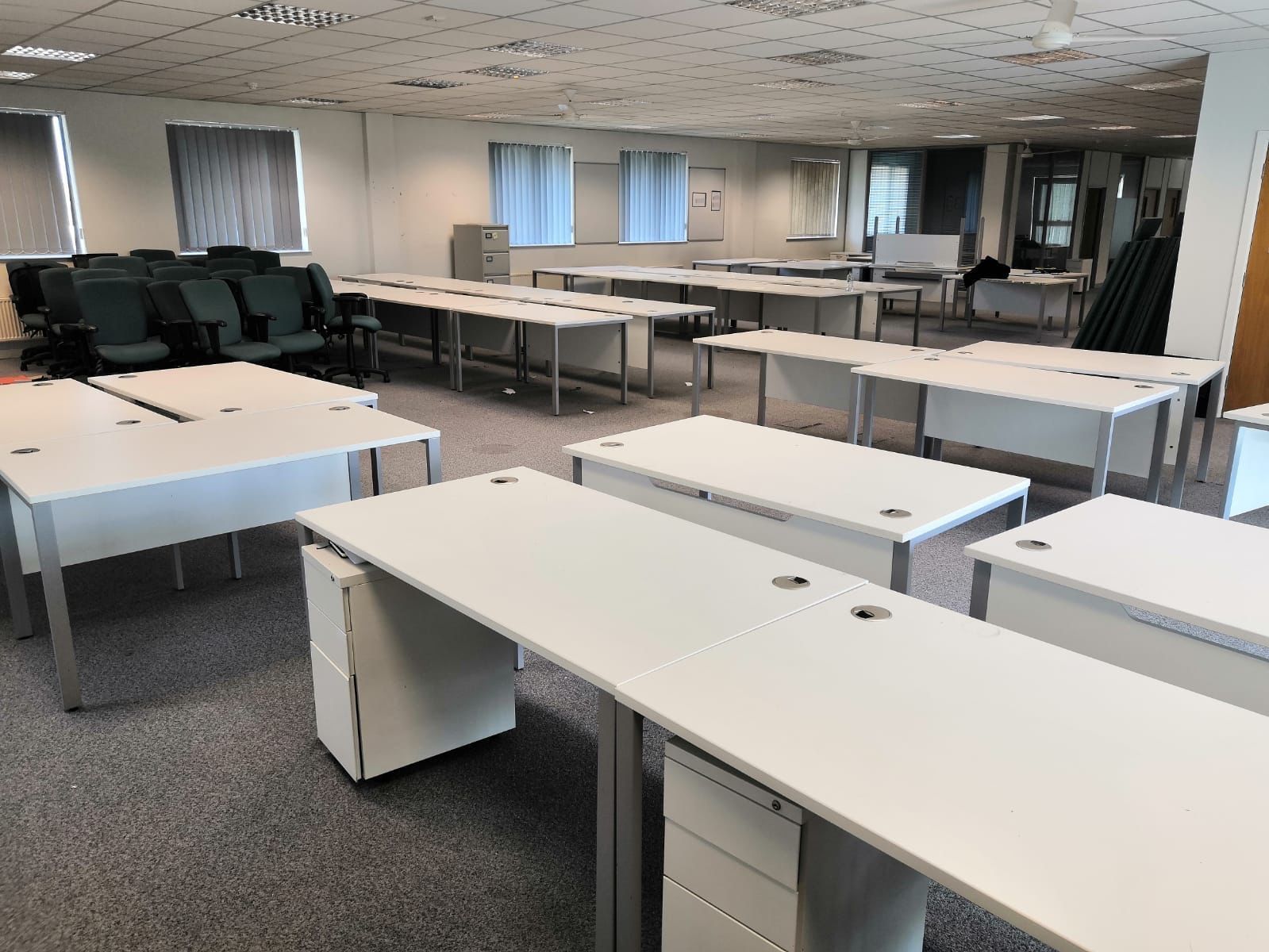 Empty office room with white desks, chairs, and windows.