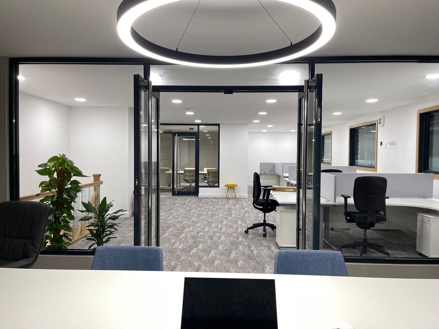 Modern office with glass walls, desks, chairs, and large circular light fixture.