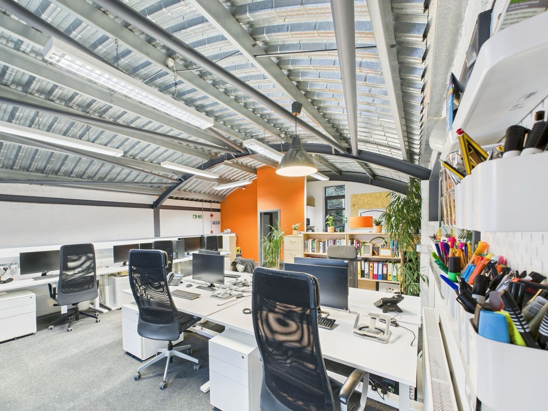 Modern office with workstations, orange accent wall, and exposed ceiling.